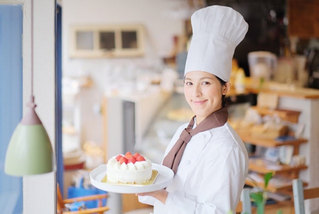 ケーキ店の店内でホールケーキを持つパティシエ