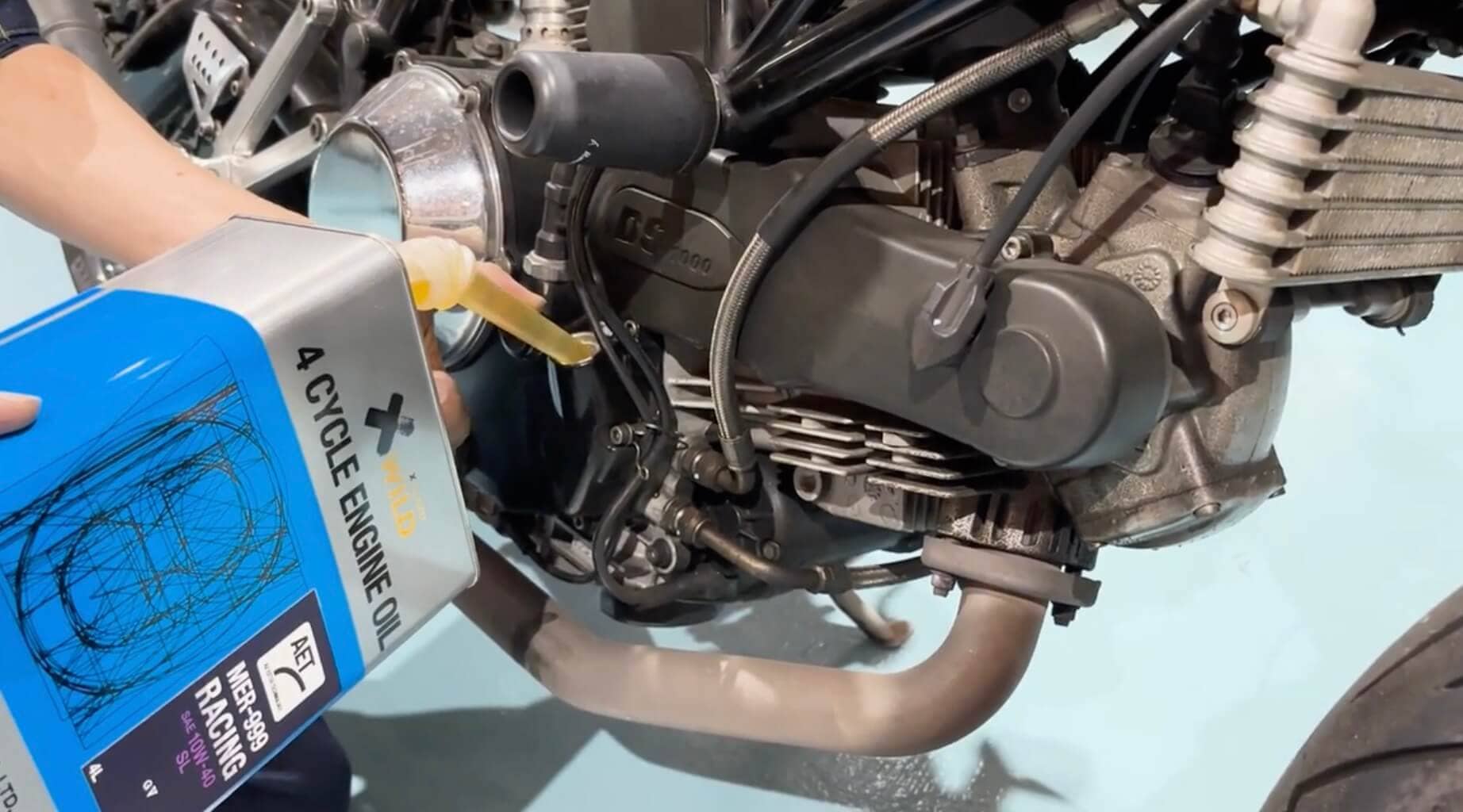 バイクのエンジンオイル注入中の様子で、青い缶に「4 CYCLE ENGINE OIL」と記載されたオイルを使用