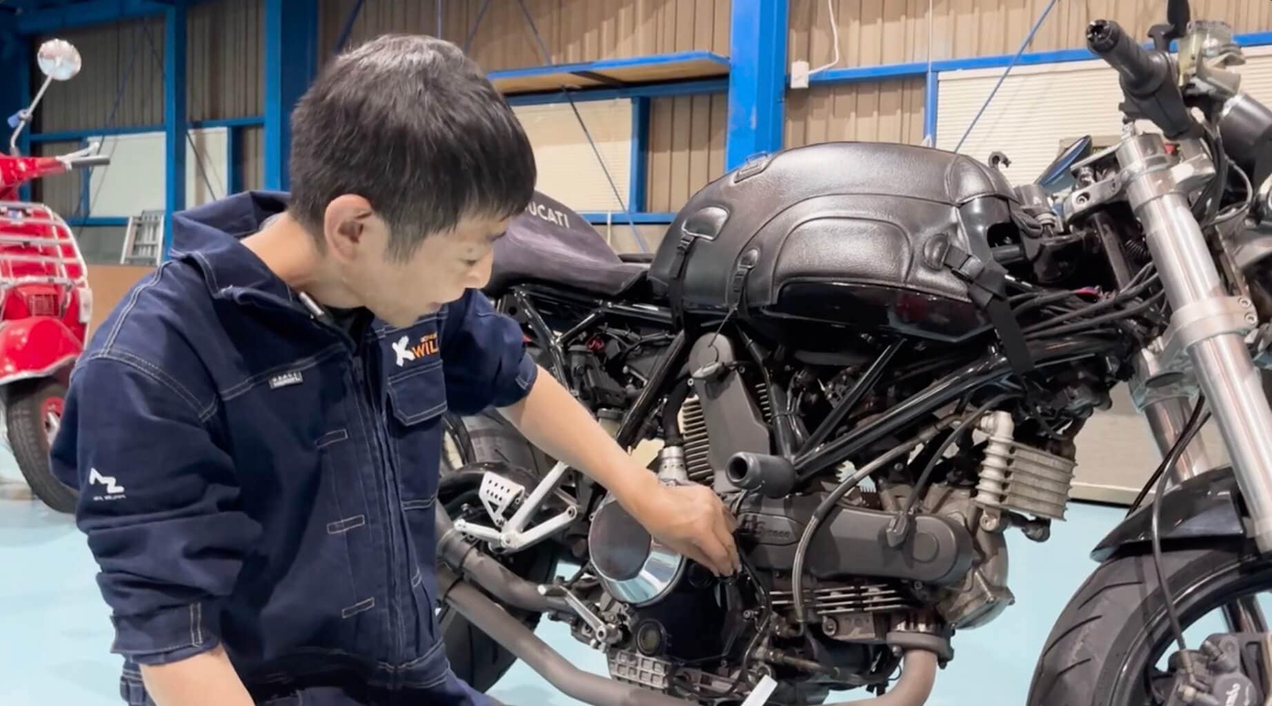 整備士がバイクのエンジン部分を指差して点検している場面