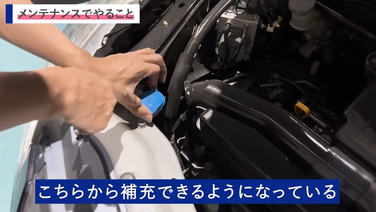 車のエンジンルーム内でウォッシャー液の補充を準備しているシーン