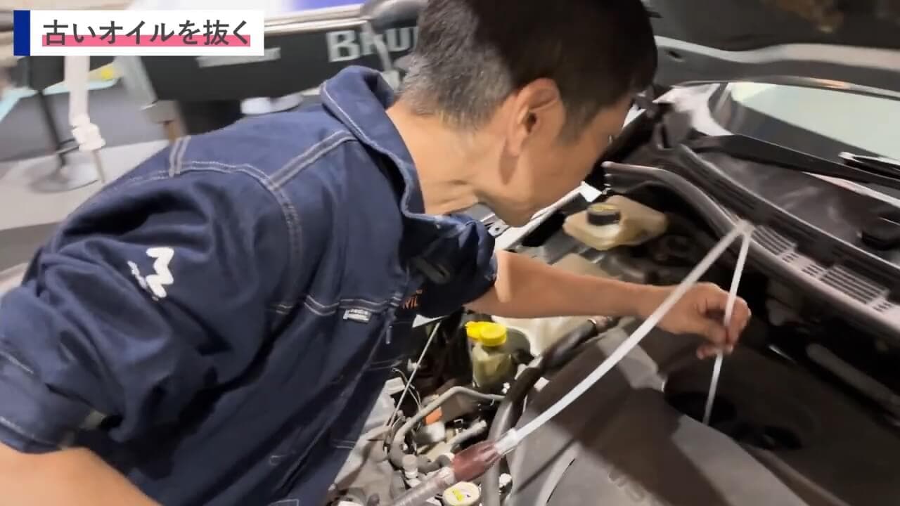 オイル交換中にホースをエンジン内部に挿入する作業のシーン