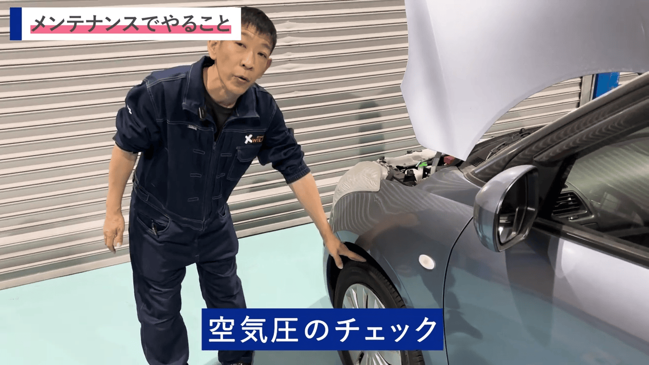 車のボンネットを開け、整備士がタイヤ部分を触れながら点検作業を行う場面