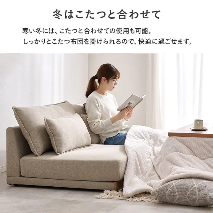 3人掛けのローソファに座り、こたつに足を入れて本を読む人