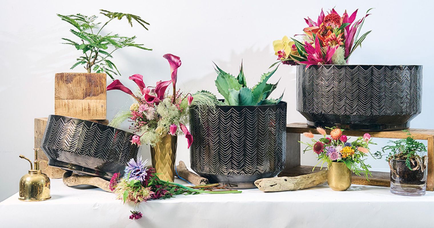 ジグザグ模様が刻まれた黒のアルミ製花器・鉢カバーに、アガベや華やかな花々、流木をあわせた卓上ディスプレイコーディネー