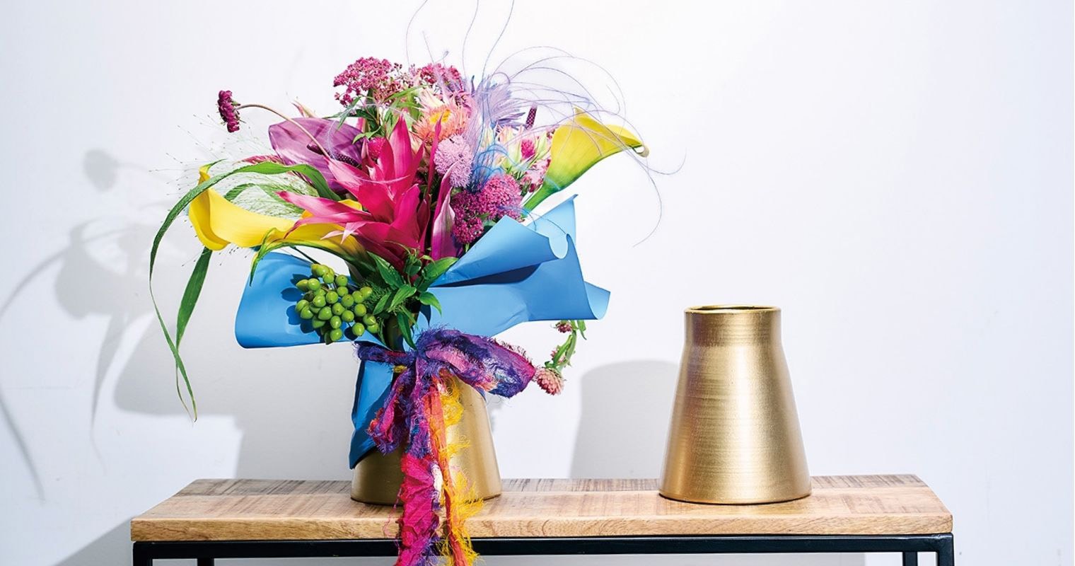 木製ラックの上に並べられたゴールドの金属製花瓶と、カラーやピンクの花をあしらった鮮やかなブーケのディスプレイ例