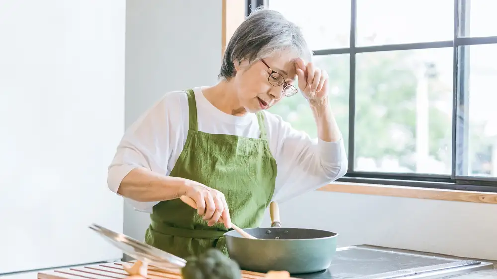 料理中に体調不良になる高齢女性の画像