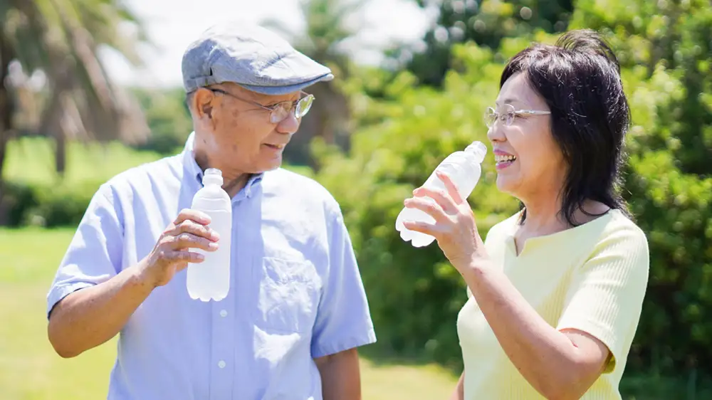屋外で水分補給をする高齢夫婦の画像