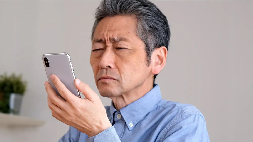 老眼でスマホの文字が読めない男性の画像