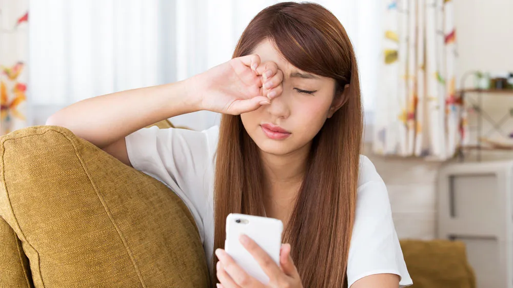 スマホ老眼なのか目元をこする若者女性の画像