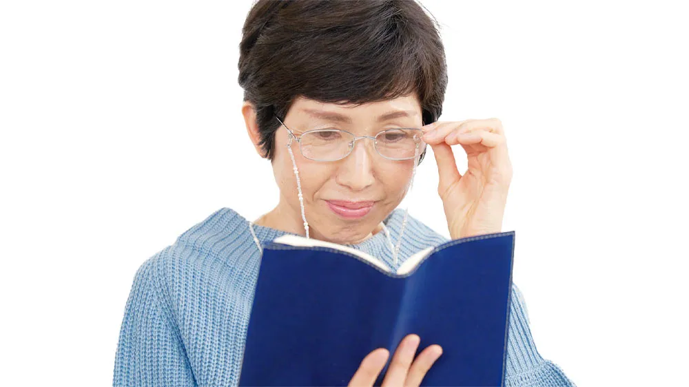 老眼鏡を使って本を読む女性の画像