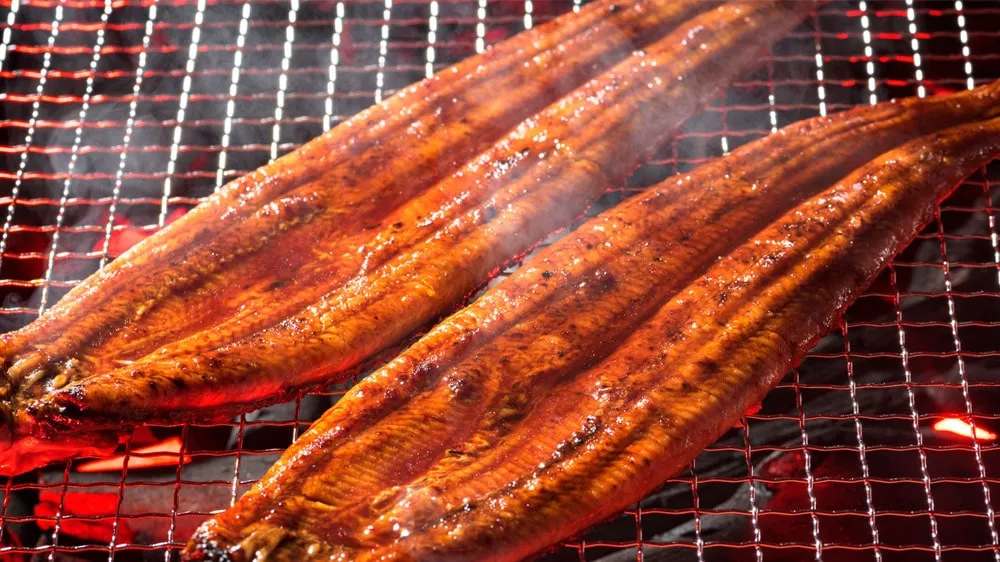 網で焼かれる鰻の蒲焼きの画像