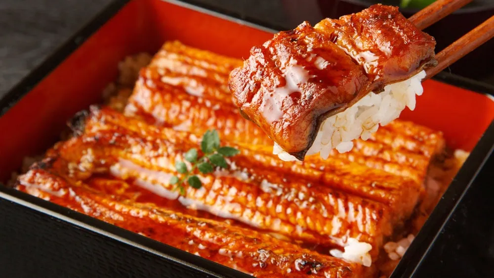 うな重から箸で持ち上げられる鰻と白米の画像