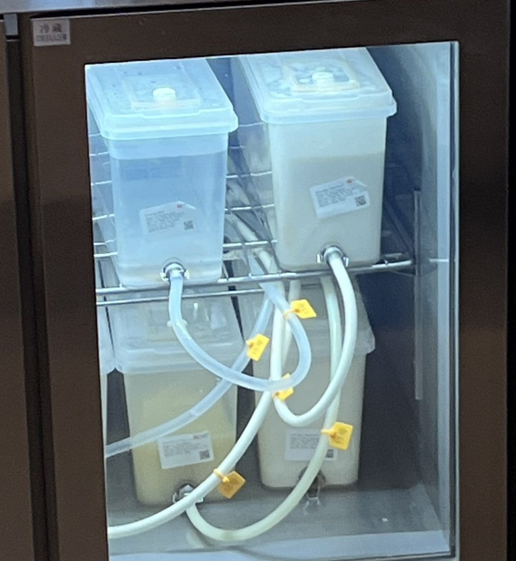 CHAGEEソウル店のカウンター下の冷蔵庫。透明な容器に白い液と黄色がかった白い液が入り、容器の口から白いチューブが機械へ伸びている