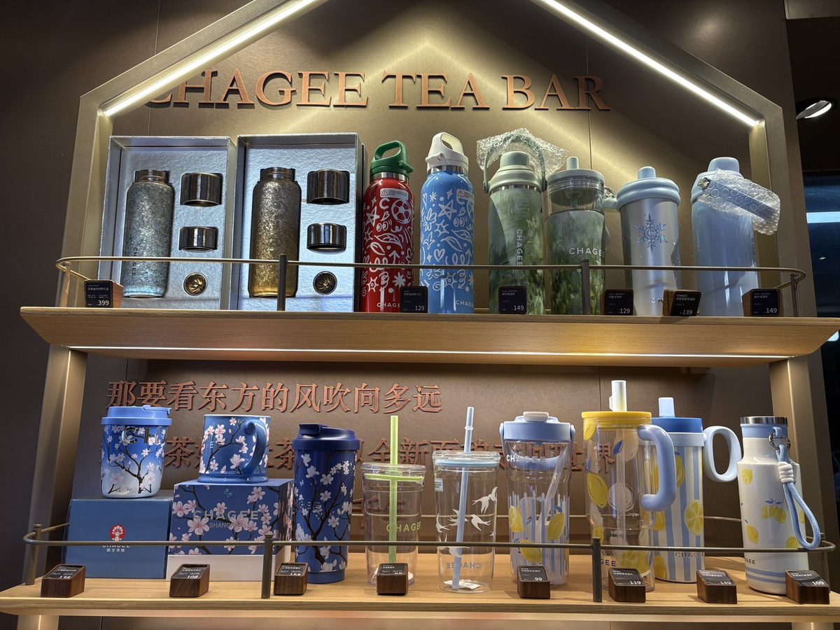 上海のCHAGEE店舗のグッズ棚「CHAGEE TEA BAR」。上段に茶器のギフトセットと色とりどりの水筒、下段に青い花柄のマグとタンブラー、レモン柄のボトルが値札付きで並ぶ