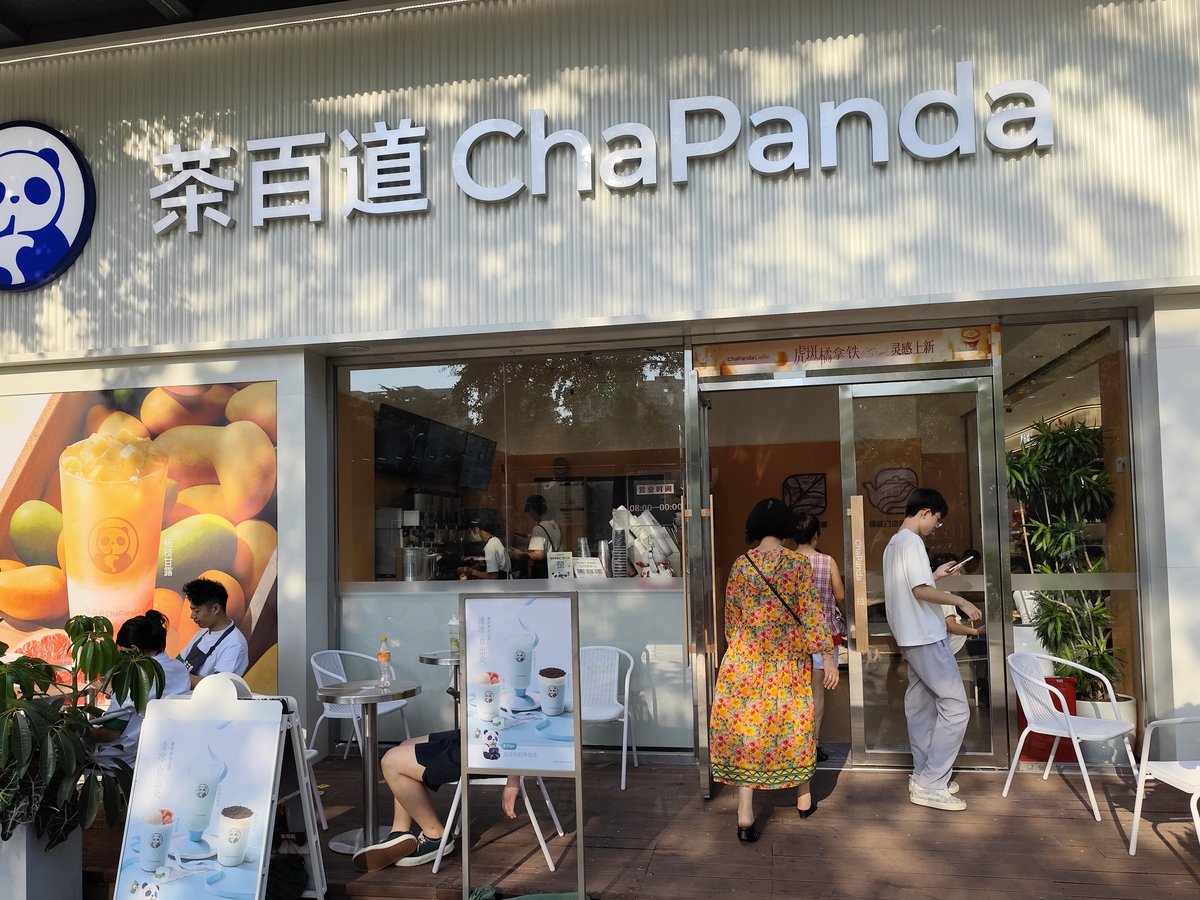 中国・深圳市の路面にある茶百道（ChaPanda）の店舗外観。白い壁に茶百道とChaPandaの立体文字、青いパンダのロゴ、マンゴーの楊枝甘露のポスターが並び、店先のテーブルで客がくつろいでいる