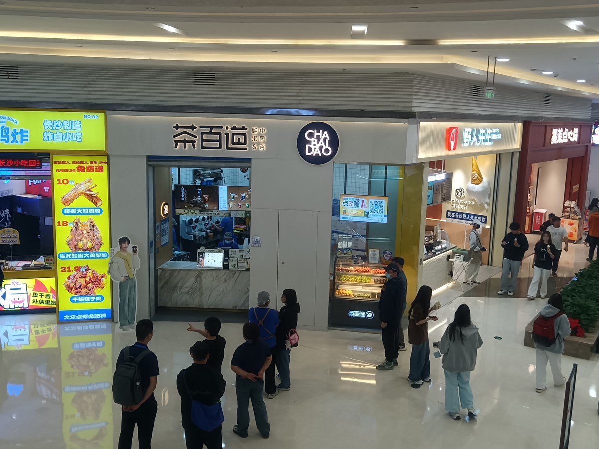 中国・長沙の商業施設にある茶百道の店舗。茶百道の看板とCHA BAI DAOの丸いロゴ、店頭の冷蔵ケースに並ぶ果物、店の前で待つ客の列