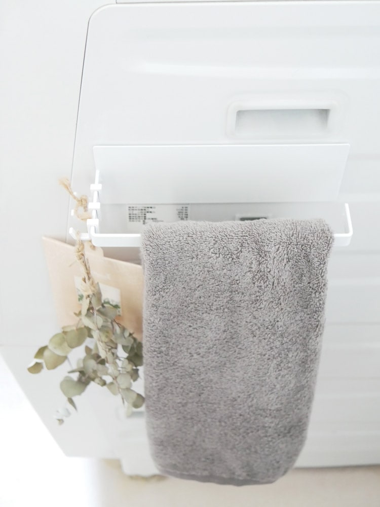 タワー製マグネットバスブーツホルダーが浴室の白いプラスチック面に取り付けられ、トイレットロールやタオルを掛けている様子