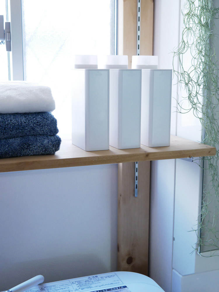 towerブランドの詰め替え用ランドリーボトルが棚に並べられ、タオルやリネンとともに展示されている