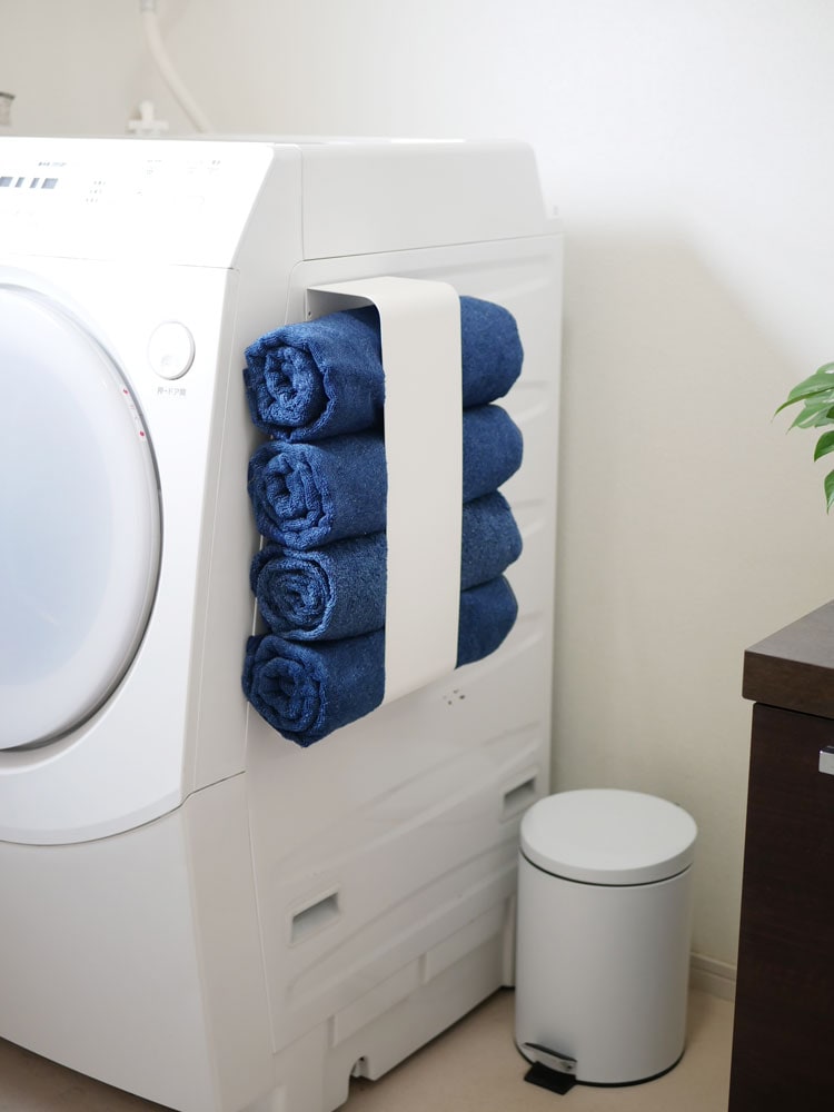 YAMAZAKIのタワー型マグネットバスタオルホルダーが洗濯室に設置され、約4枚のバスタオルを掛けている様子