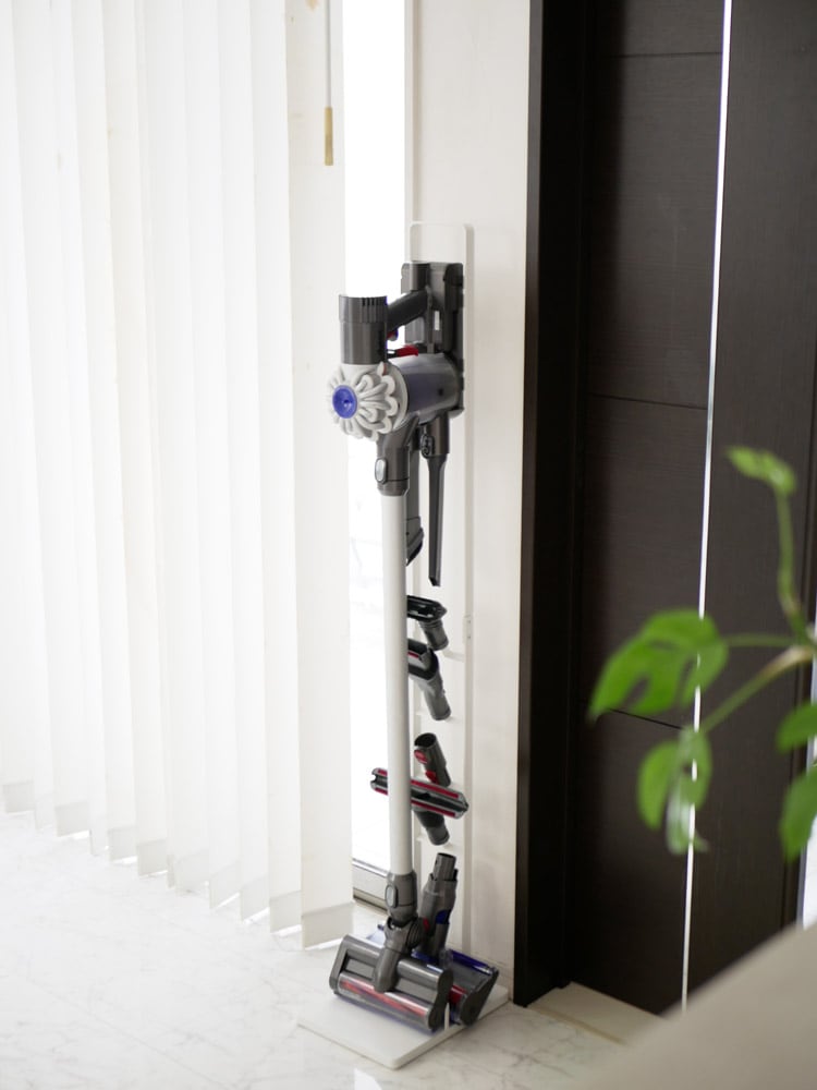 タワーのコードレスクリーナースタンドが木製床の上に設置され、ダイソン掃除機を固定している様子