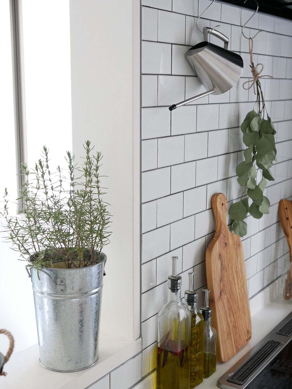 ステンレス製SALUSミッテジョーロがキッチンのカウンターに置かれ、花鉢や果物とともに整然と配置されている様子