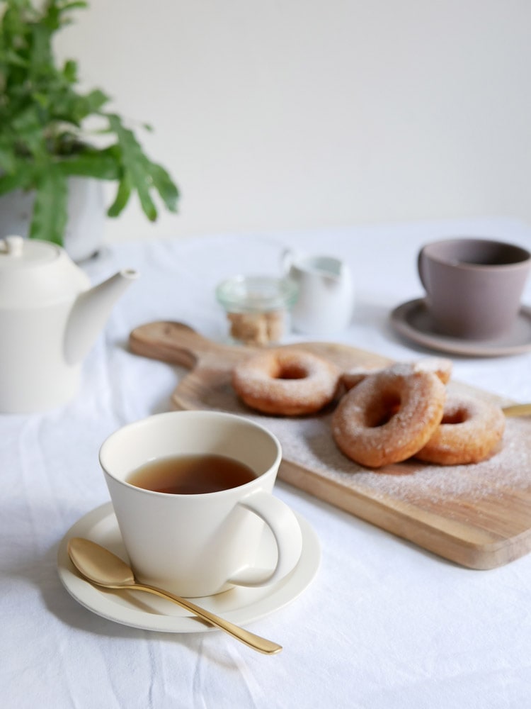 SAKUZAN Saraシリーズのクリーム色磁器製コーヒーカップとソーサーのセットがテーブルに並べられている様子