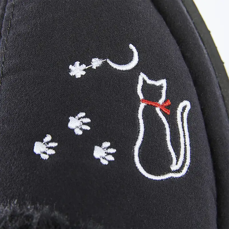 サンダルの甲に施された、赤いリボンを付けた白猫と足跡の刺繍のクローズアップ。