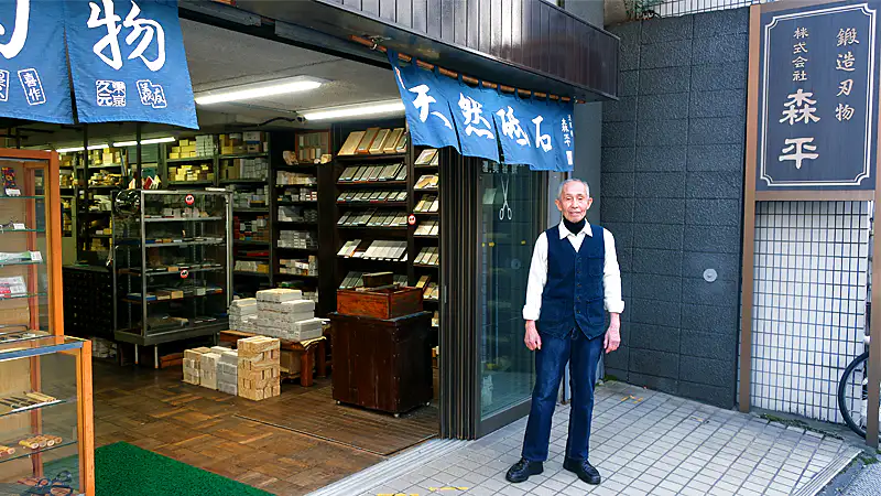 東京・浅草橋で昭和8年（1933年）から続く、刃物と天然砥石の専門卸問屋「森平」の外観と小黒章光さんです。長年培った知識と経験が、人造砥石 火シリーズに注ぎ込まれています。
