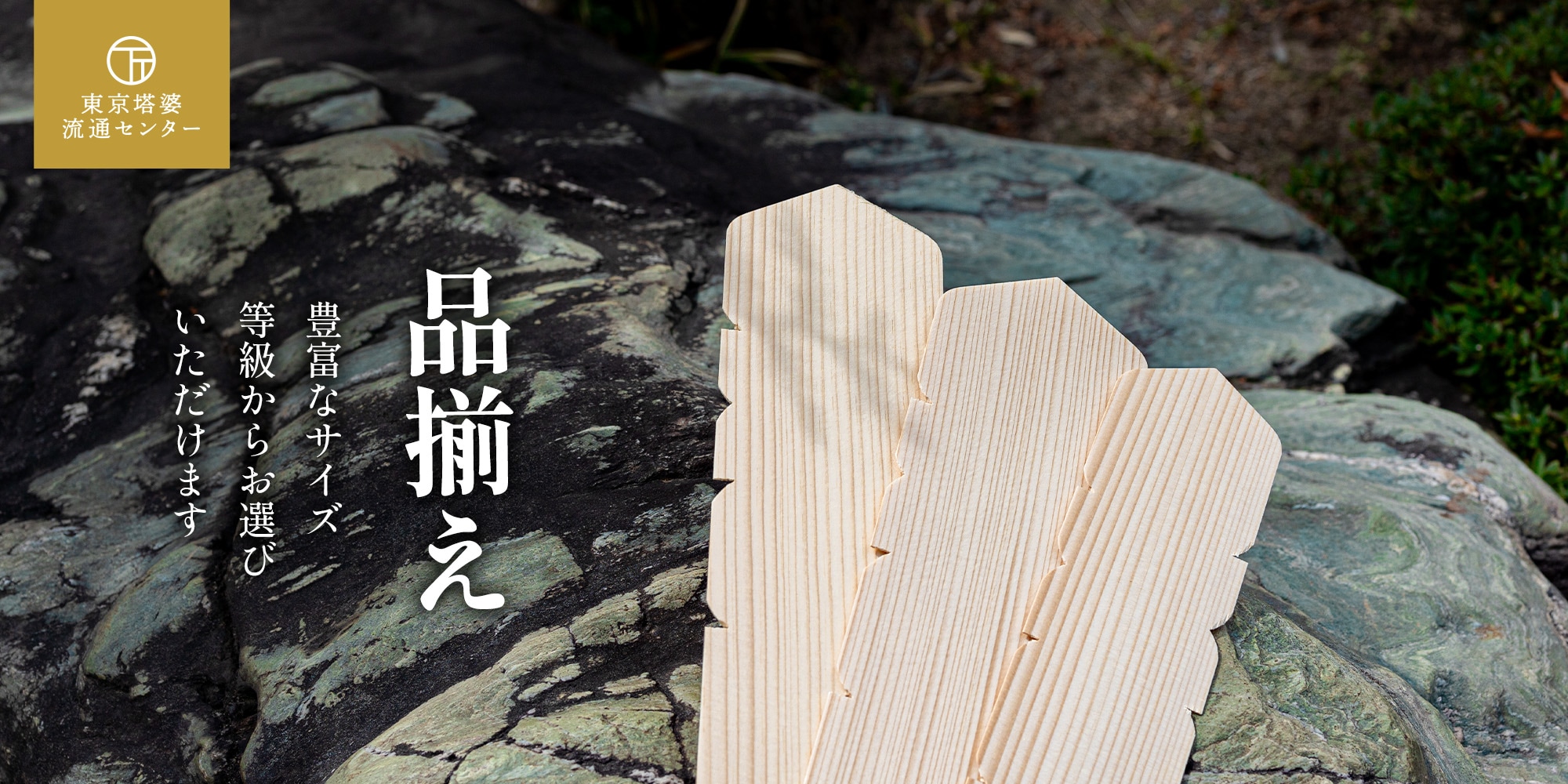 東京塔婆流通センターの卒塔婆、卒塔婆の背景に自然岩と植栽が写っている。豊富なサイズや等級をお選びいただけます。