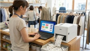 アパレル店舗のバックヤードでラベルプリンターとパソコンを操作するスタッフ