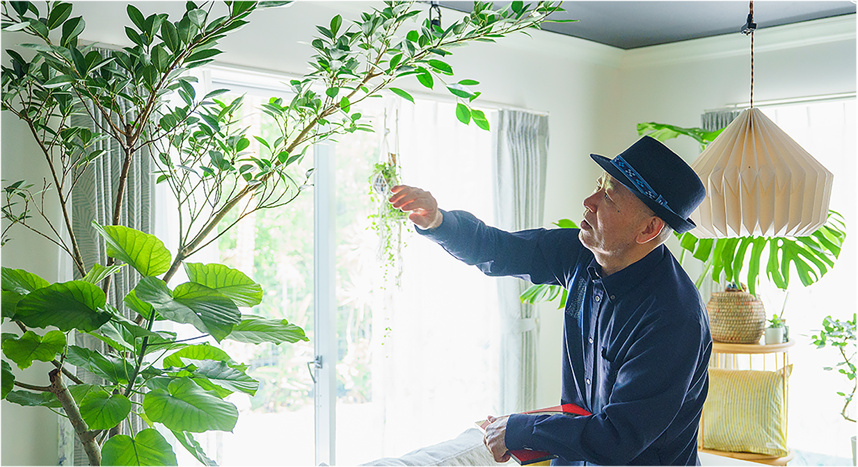 天井近くの植物の葉に触れる和来龍先生の写真