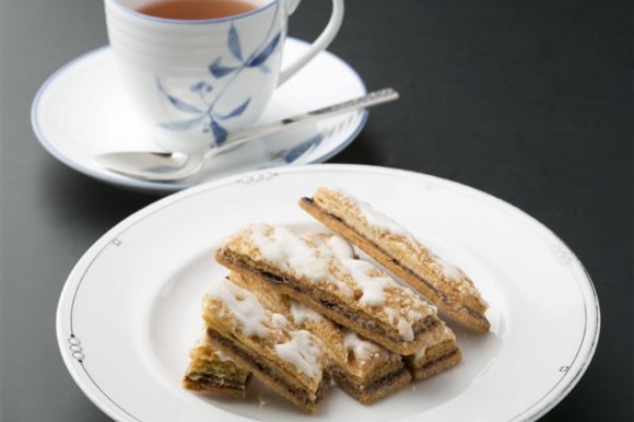 白い皿に重ねて盛り付けられた、細長く焼き上げられた雪吊り（YUKIZURI）。パイ生地とクッキー生地の層に梅の餡が挟まれ、上から白いアイシング（またはフォンダン）がかけられている様子。