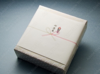 淡い色の和柄の包装紙に包まれ、その上から白い掛け紙（のし）がかけられた、丁寧にラッピングされた贈答品の箱。中央に『お礼』のような文字が書かれており、紅白の細い水引が結ばれている様子