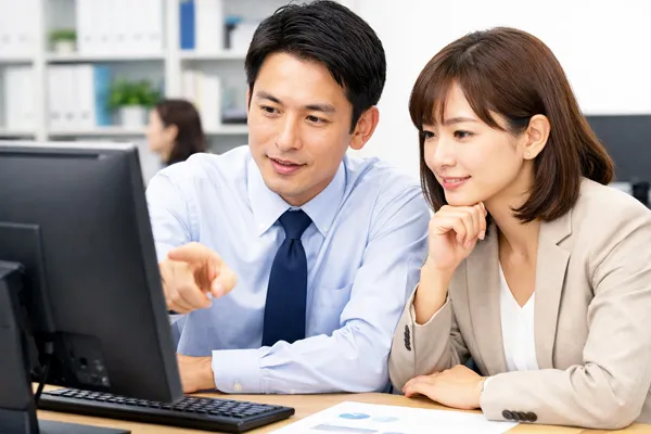 法人PC選定について担当者2人が画面を見ながら相談するシーン