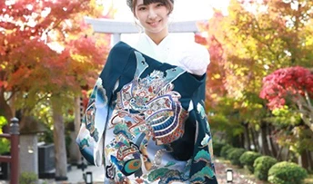 紅葉を背景に、華やかな着物を着て微笑む女性