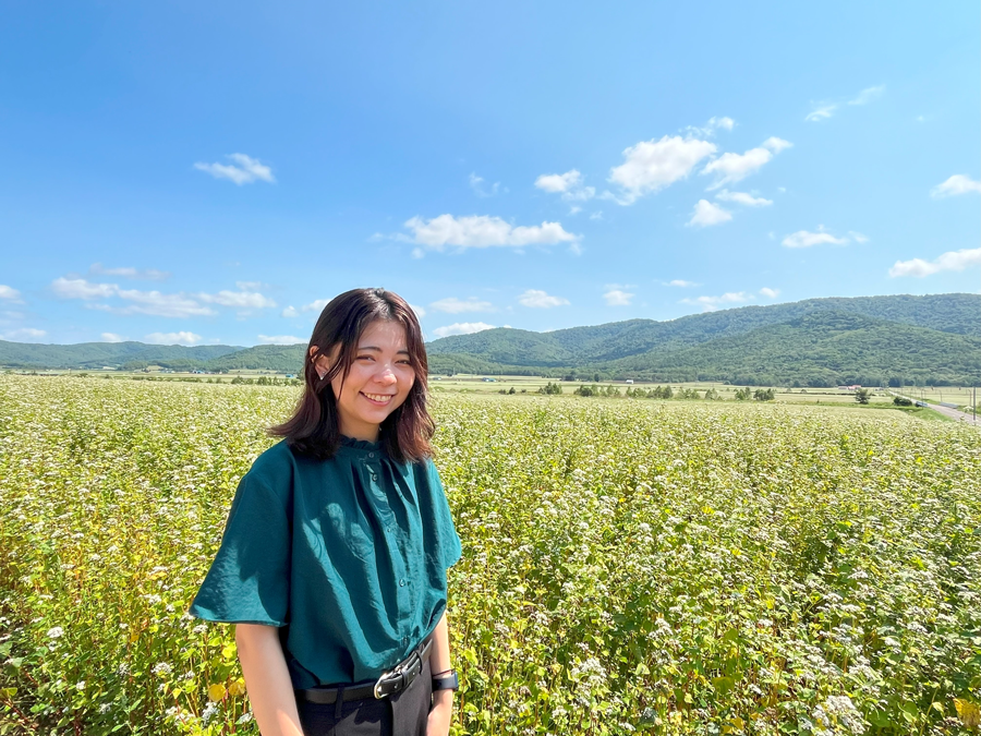 トヅキ合同会社の石川さん、一面に咲くそばの花畑の前で