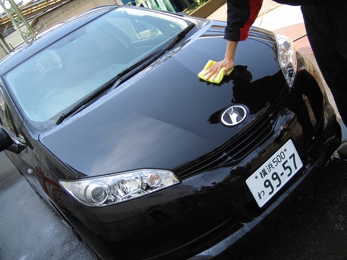 黒い車のボンネットを黄色いクロスで拭いている様子