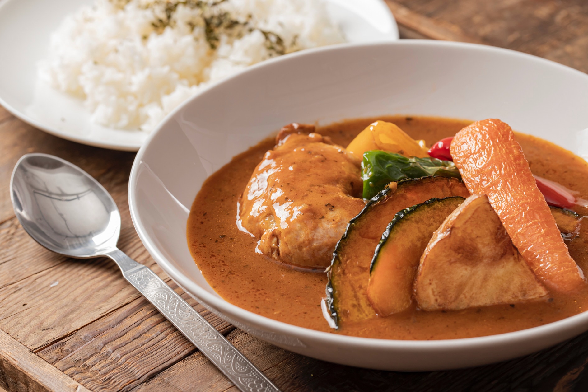 スープカリィ侍のレトルト商品「骨付きチキンのスープカレー」を調理して皿に盛り付ける,具材たっぷりのスープカレー・ライス・スプーン